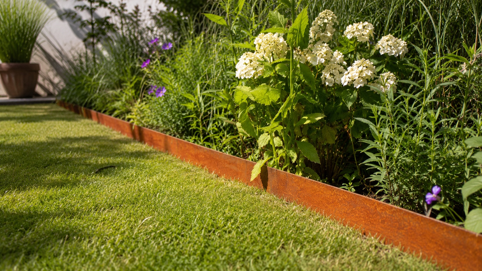 Eine Beeteinfassung aus Cortenstahl trennt den Rasen sauber vom bepflanzten Gartenbeet.