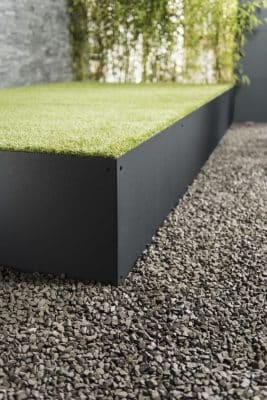 Eine Terrasse aus Schwarzstahl bildet den Rahmen für eine sauber verlegte Fläche aus Kunstrasen.
