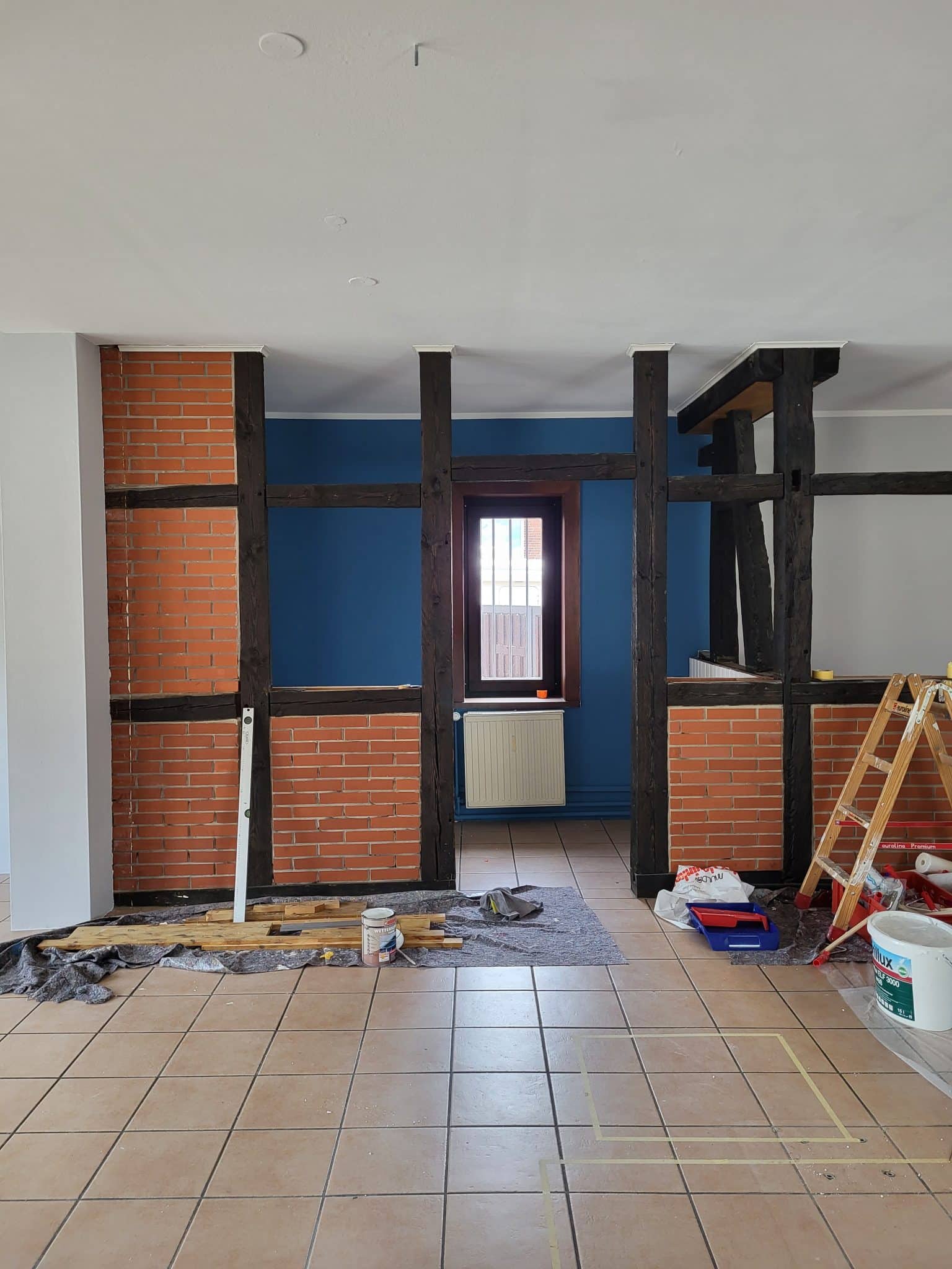 In einem Raum mit einer Fachwerkwand aus Backstein sowie einer blauen Wand laufen Renovierungsarbeiten.
