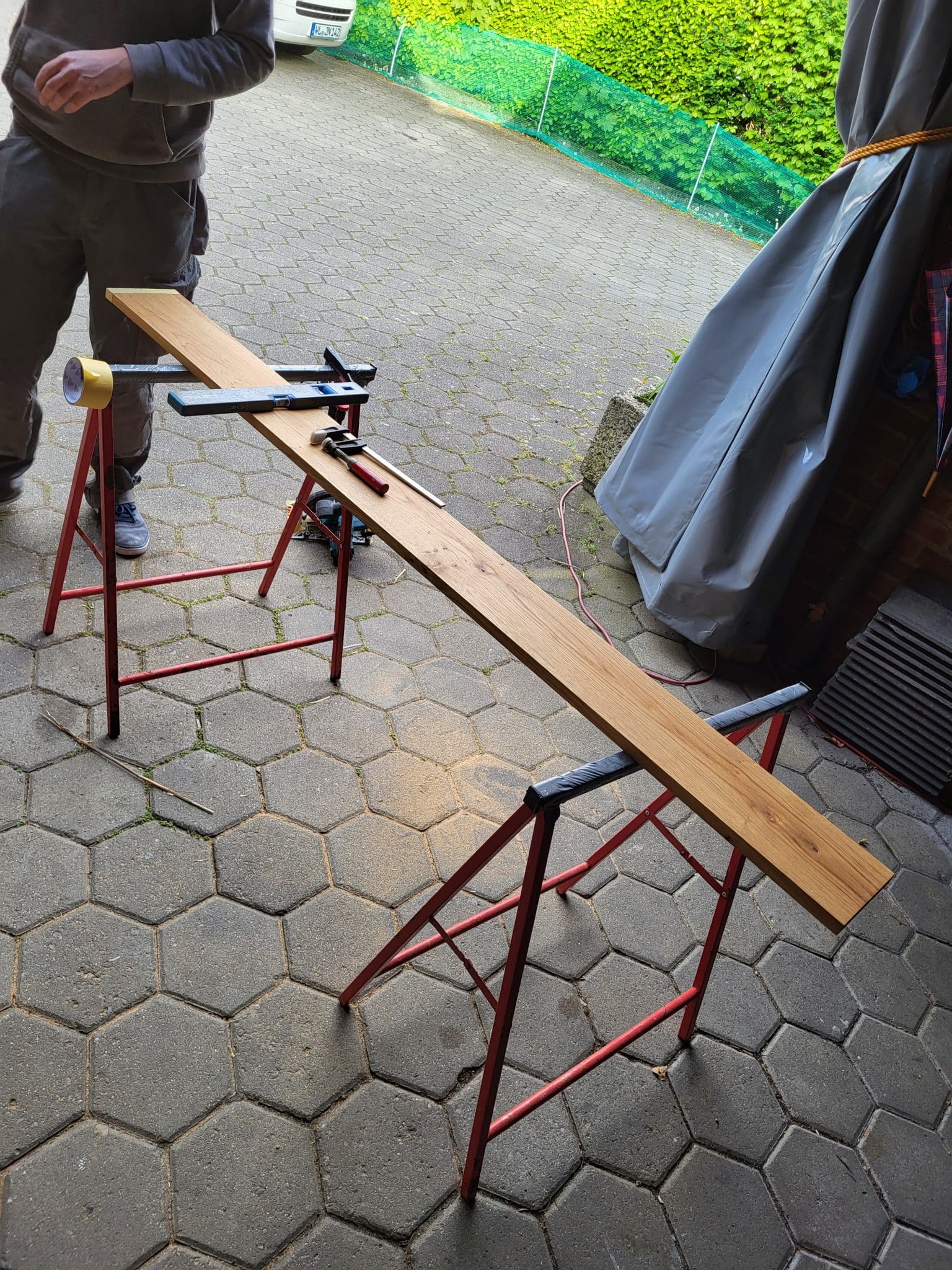 Ein Holzbrett liegt zur Bearbeitung auf zwei Böcken und vorbereitetem Werkzeug.