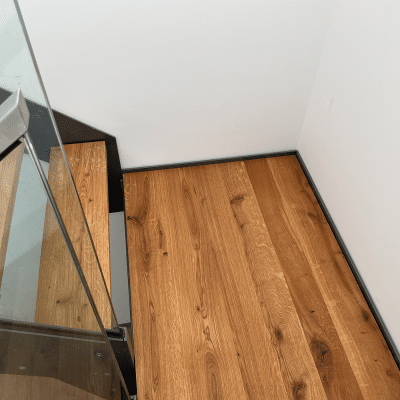 Eine Treppe mit Holzstufen, schwarzem Stahlrahmen und Glasgeländer ist aus seitlicher Perspektive zu sehen.