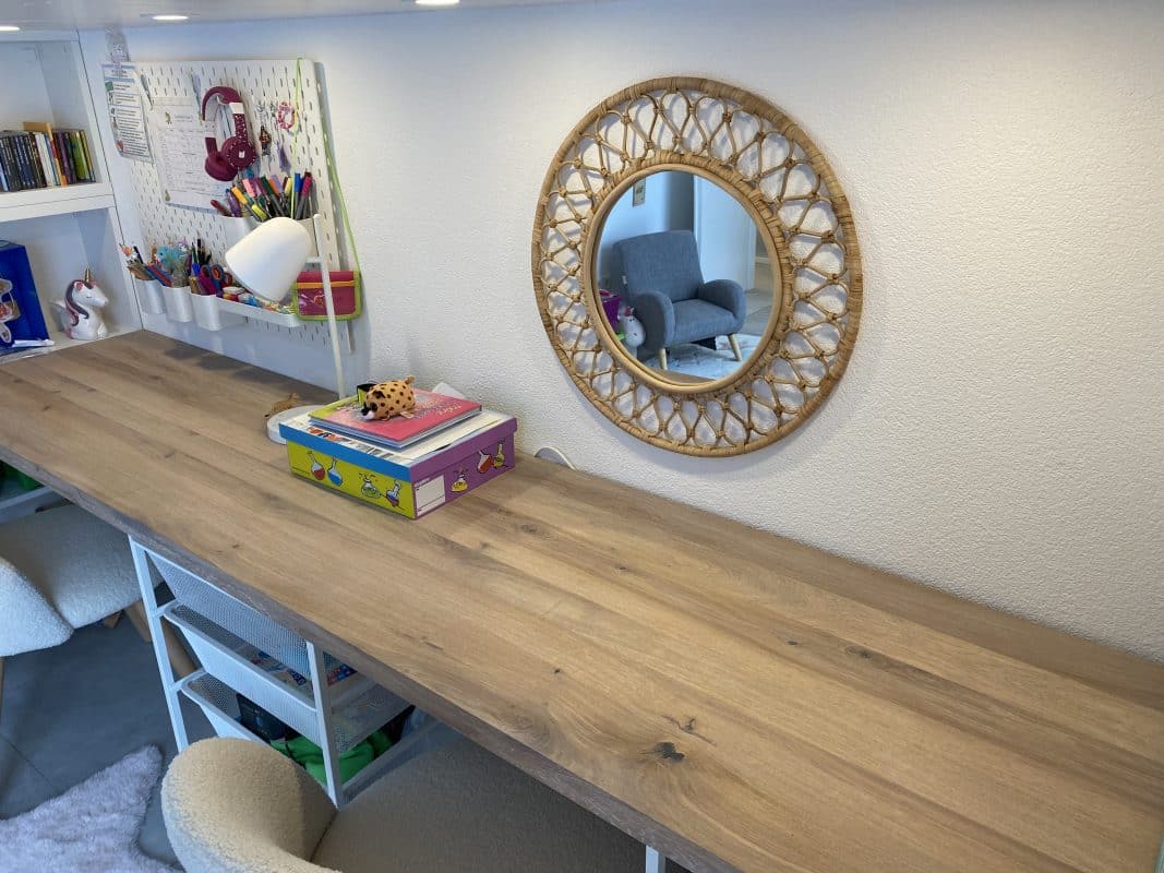 Kinderspielbereich mit Holzschreibtisch und rundem Rattanspiegel.