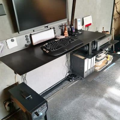 Ein schwarzer Schreibtisch mit Monitor und Zubehör ist ordentlich in einem Arbeitsraum moniert.