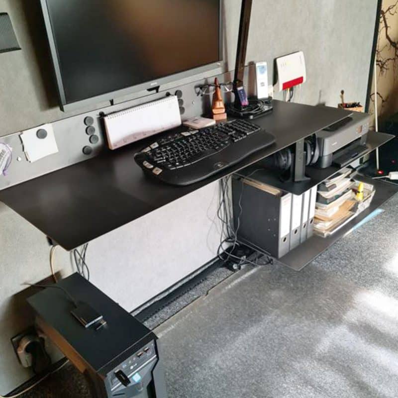 Ein schwarzer Schreibtisch mit Monitor und Zubehör ist ordentlich in einem Arbeitsraum moniert.