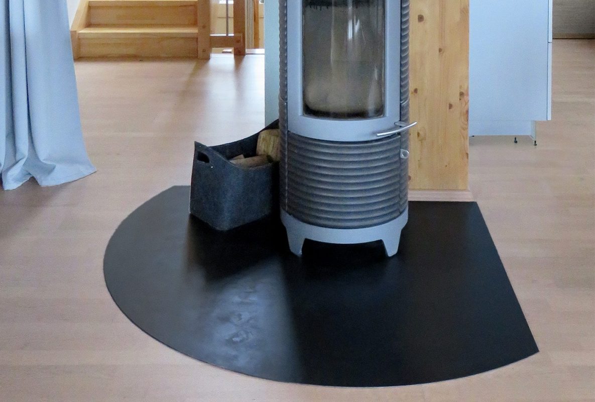 Eine runde schwarze Funkenschutzplatte schützt den Boden unter einem modernen Holzofen.