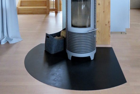 Eine runde schwarze Funkenschutzplatte schützt den Boden unter einem modernen Holzofen.