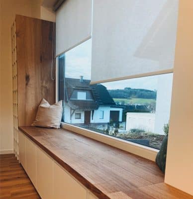 Eine breite Fensterbank aus Eiche zeigt Kissen und eine weite Aussicht.
