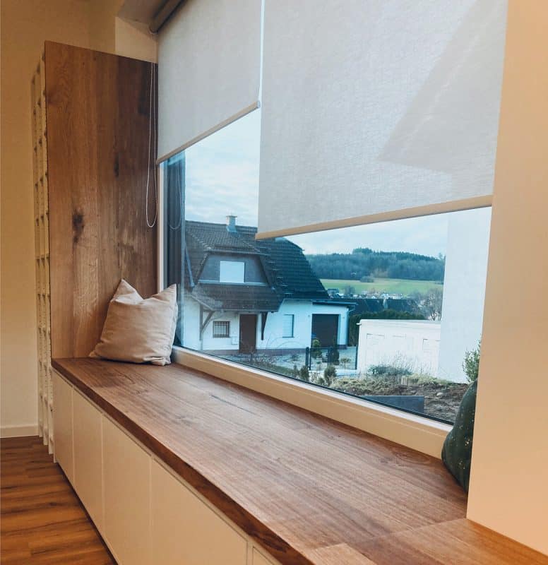 Eine breite Fensterbank aus Eiche zeigt Kissen und eine weite Aussicht.