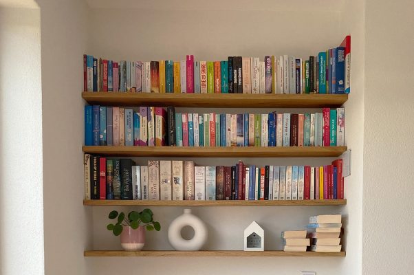 Ein Wandregal trägt zahlreiche Bücher und dekorative Objekte in einem Wohnraum.
