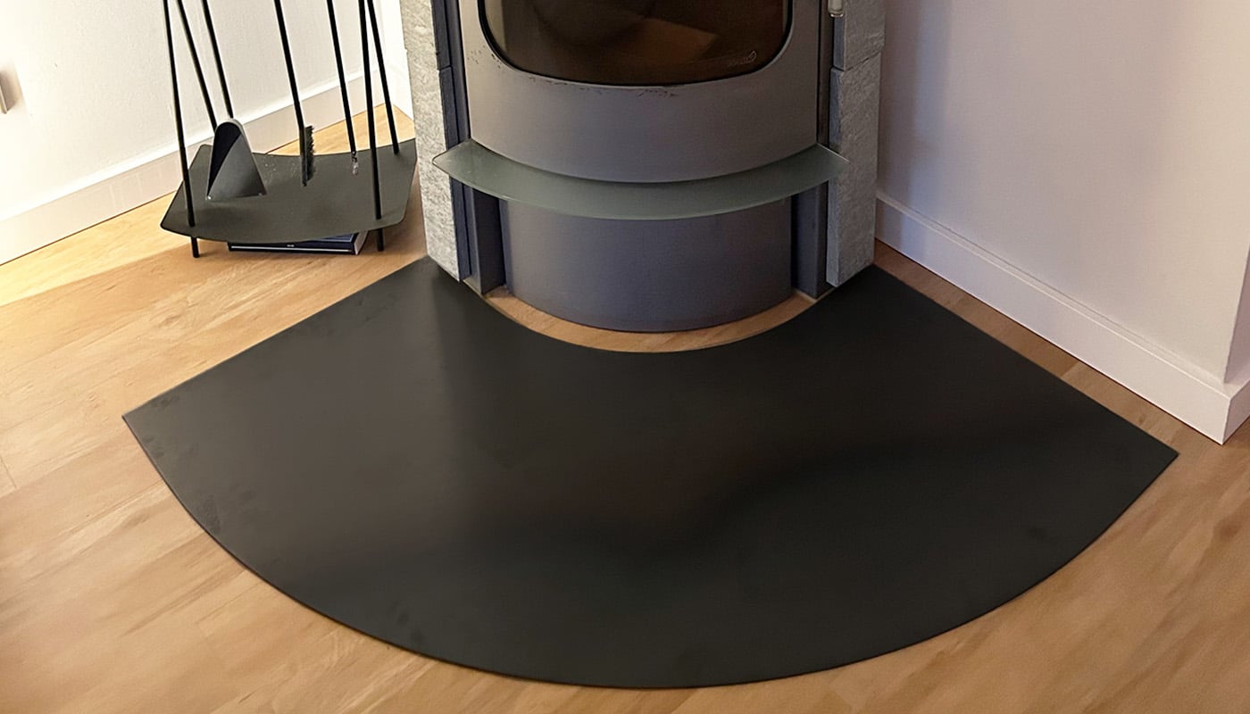 Eine schwarze Kaminbodenplatte liegt halbrund vor einem modernen Kamin.