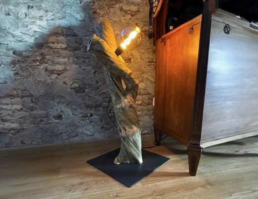 Eine Holzskulptur steht beleuchtet auf einer dunklen Metallplatte.