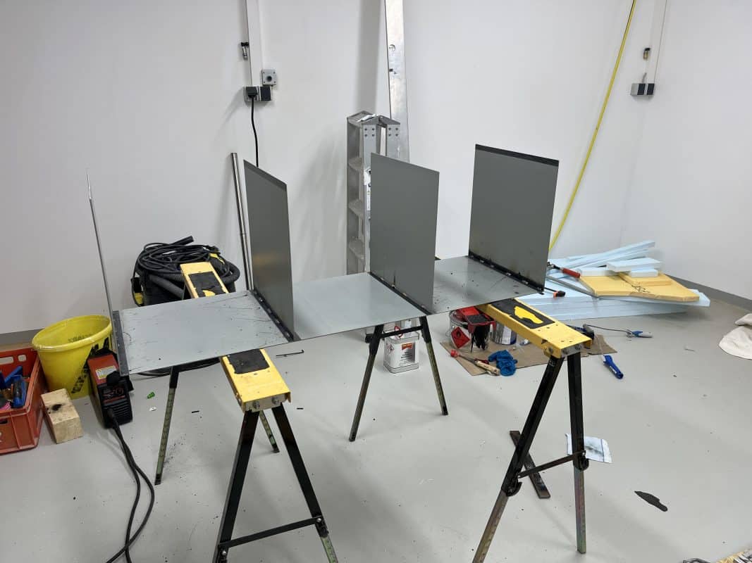 Ein Werkraumaufbau zeigt zugeschnittene Metallplatten auf zwei Arbeitsböcken.