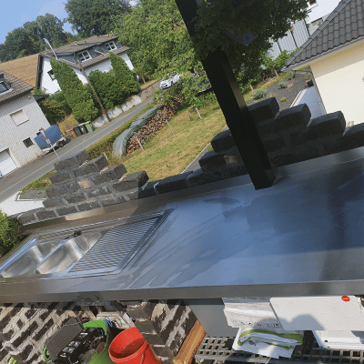 Eine Outdoor-Edelstahlküche ist in einem Außenbereich mit Blick auf Wohnhäusern montiert.