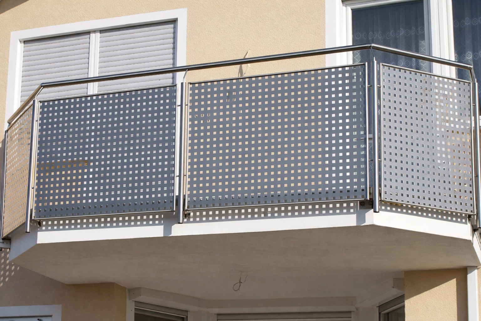 Ein moderner Balkon mit Edelstahlgeländer und quadratischem Lochblech ist an einem beigen Wohnhaus angebaut.