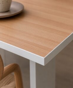 Eine helle Premium+ Tischplatte in Holzoptik mit weißem Kantendekor ist neben einem Holzstuhl und einer Tasse zu sehen.