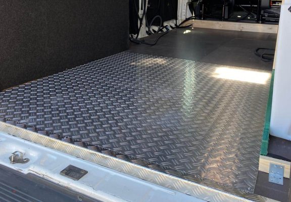 Ein Aluminium-Riffelblechboden legt die stabile Basis des Camper-Ausbaus, während die Wandkonstruktion bereits vorbereitet ist.