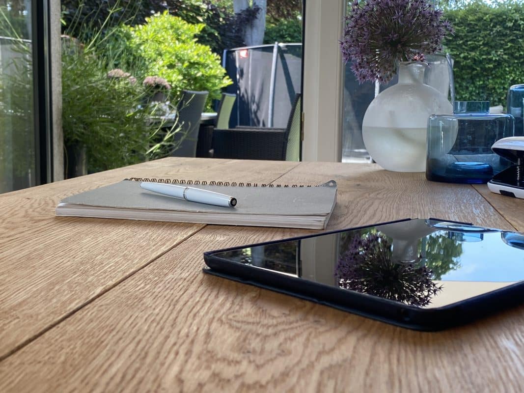 Notizbuch, Tablet und Vase auf Holztisch im Homeoffice.