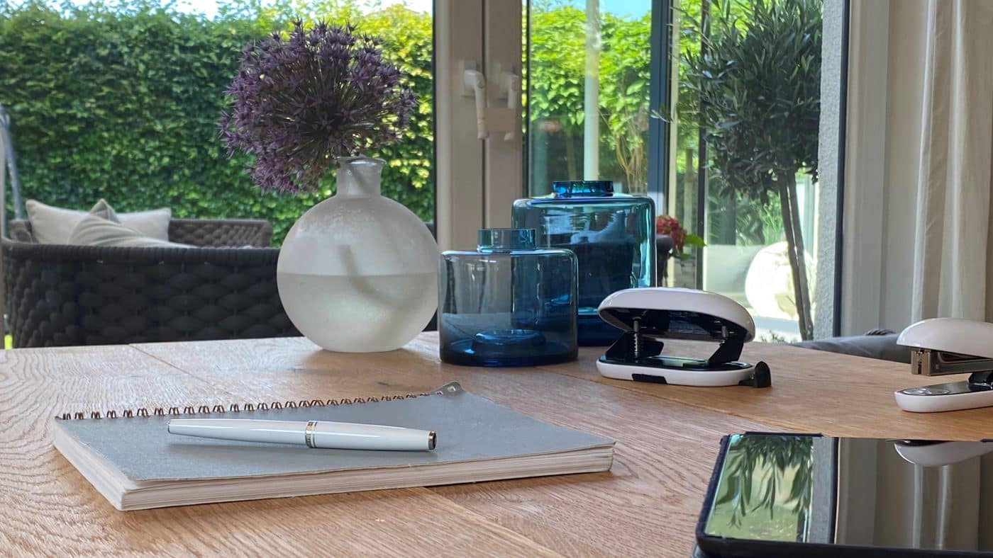 Heller Homeoffice-Platz mit Notizbuch, Vase und blauen Glasgefäßen.