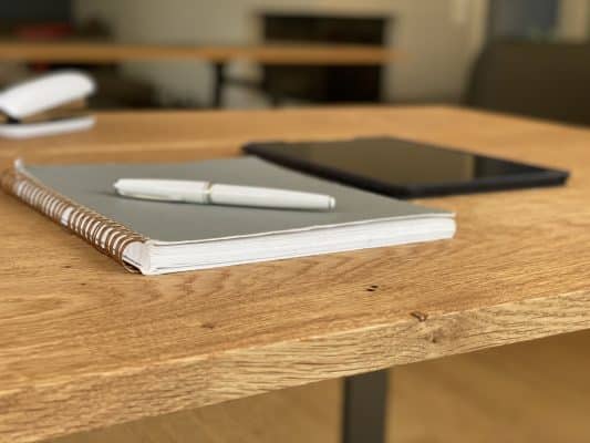 Ein Notizbuch und ein Stift liegen ordentlich auf einer Eichentischplatte.