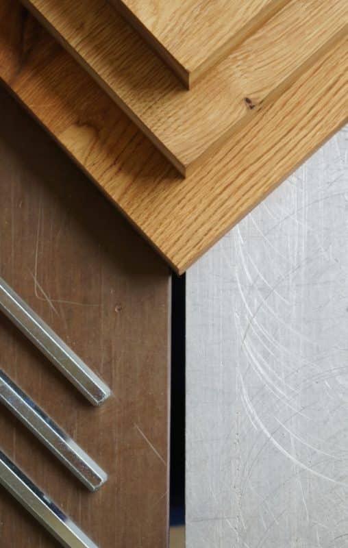 Die Holzplatte trifft auf eine matt verkratzte Metallfläche im Detail.