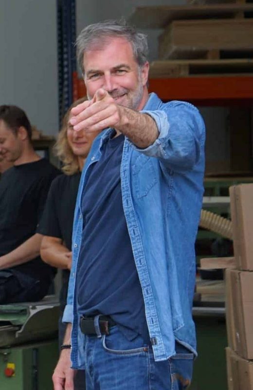 Ein Mann in Jeansjacke zeigt lächelnd nach vorne in die Kamera.