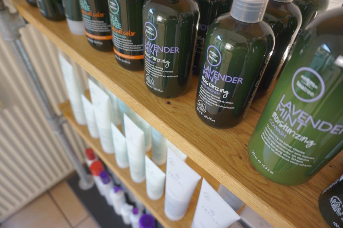 Haarpflegeprodukte in grün-weißen Flaschen auf einem Holzregal im Salon.
