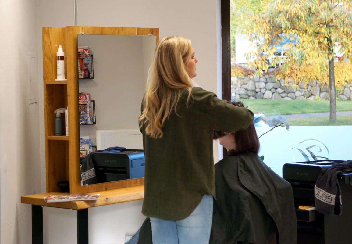 Friseurin arbeitet an Kundin vor einem großem Spiegel mit Holzrahmen.