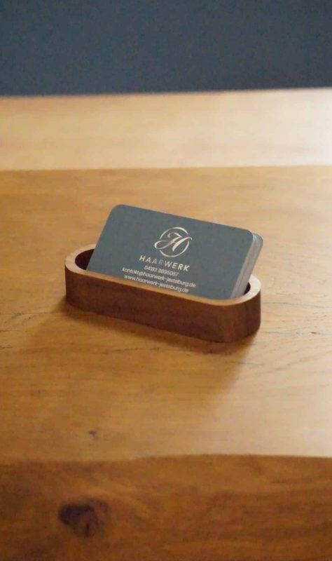 Haarwerk-Visitenkarten in einer kleinen Holzschale auf einem Holztisch.