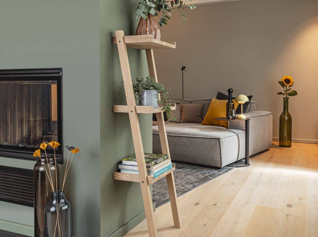 Modernes Wohnzimmer mit grüner Wand, Holzleiterregal und grauem Sofa.