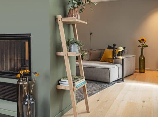 Ein hohes Holzregal mit Pflanzen steht ist in einem modernem Wohnzimmer platziert.