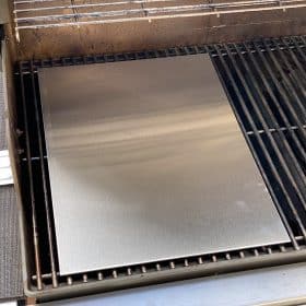 Eine Edelstahlplatte liegt sauber auf einem Grillrost und reflektiert das Licht.