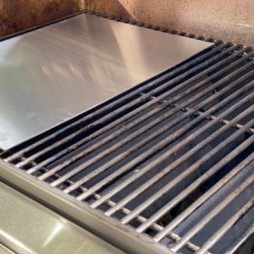 Detailaufnahme einer Edelstahl-Grillplatte auf einem Grillrost, gefertigt nach Maß.