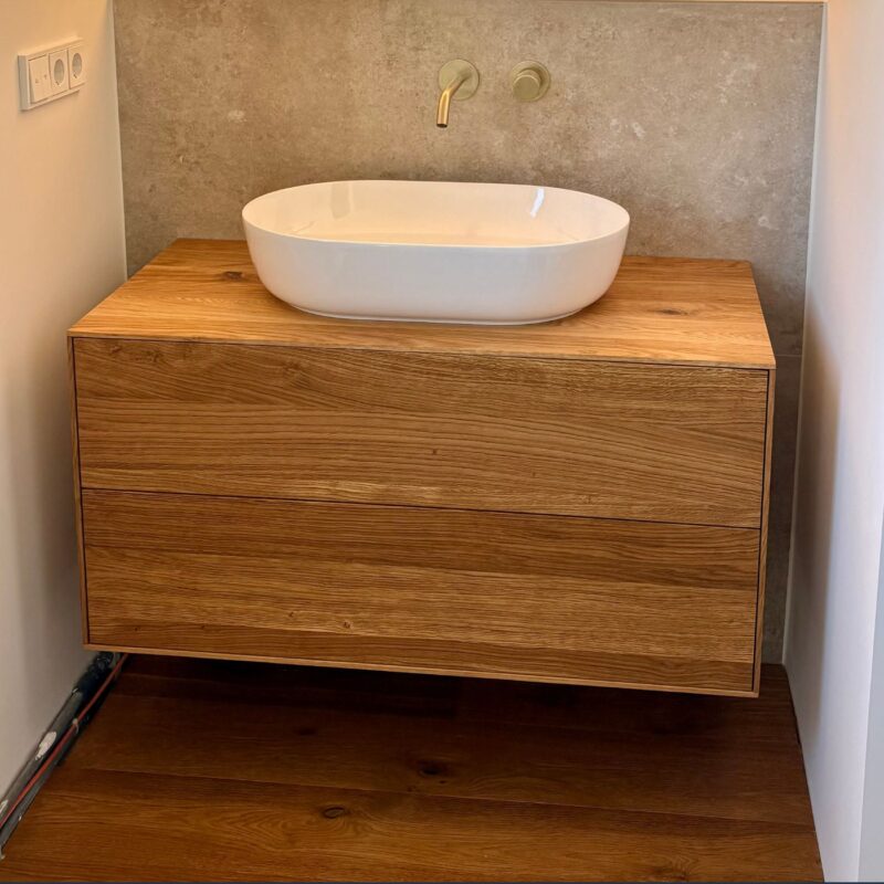 Ein Waschtisch aus Eiche trägt ein weißes Aufsatzwaschbecken im modernen Bad.