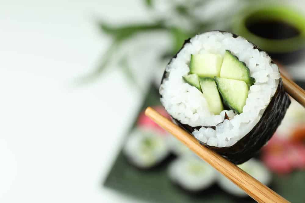 Sushi-Makirolle mit Gurkenfüllung wird von Essstäbchen gehalten.