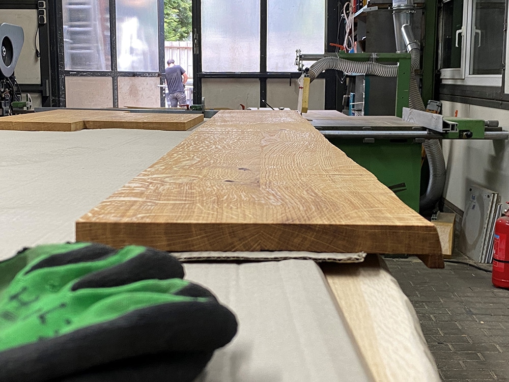 Eine Holzbohle liegt auf einer Maschine in einer Werkhalle.