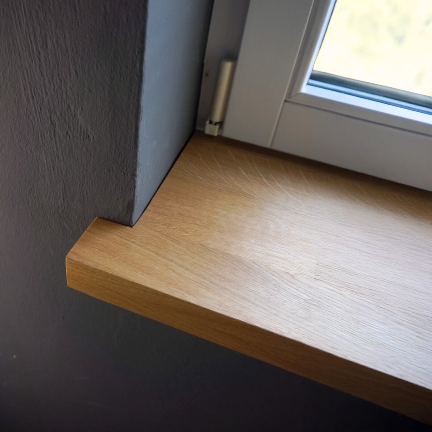 Fensterbank aus massiver Eiche, glatt geschliffen, mit natürlicher Maserung, montiert unter einem Fenster im Innenraum.
