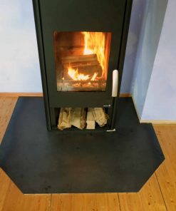 Eine kantige Funkenschutzplatte liegt vor einem brennenden Kamin auf hellem Holzboden.