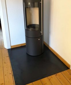 Eine schwarze Funkenschutzplatte liegt passgenau in einer Raumecke auf dem Holzboden.