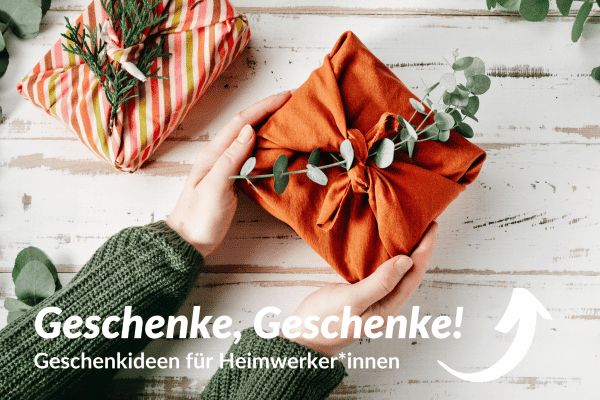 Zwei Hände halten ein in Stoff verpacktes Geschenk mit grünem Zweig.
