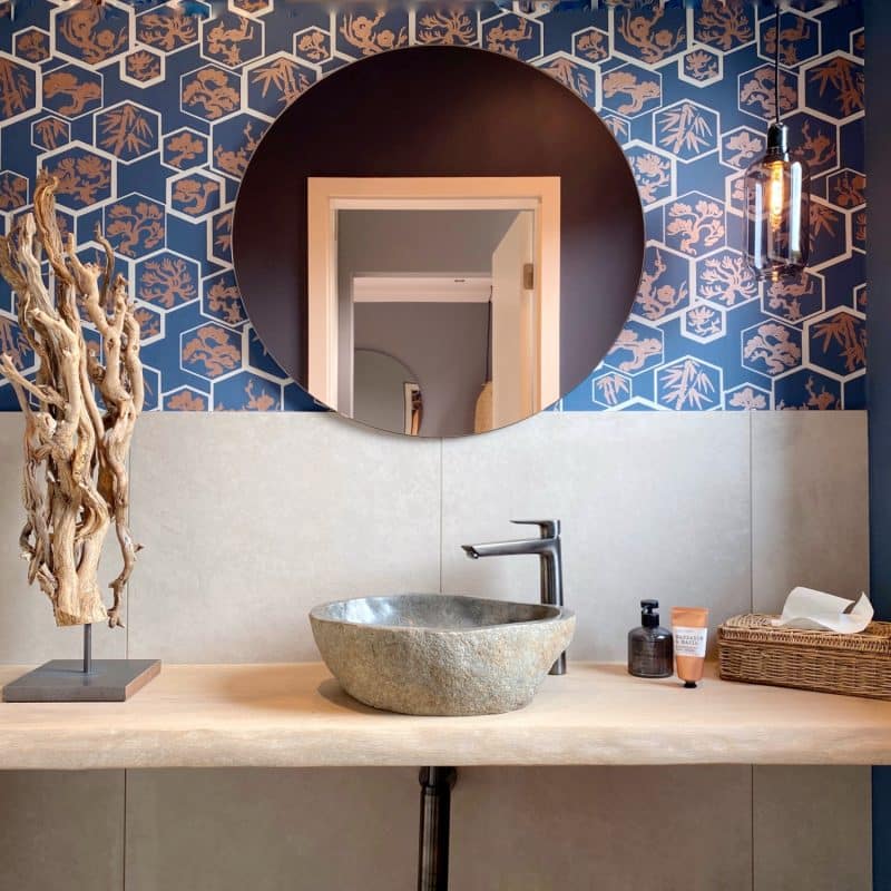 Modernes Badezimmer mit Holzwaschtisch, Steinwaschbecken, runder Spiegelwand und blauer Muster-Tapete.