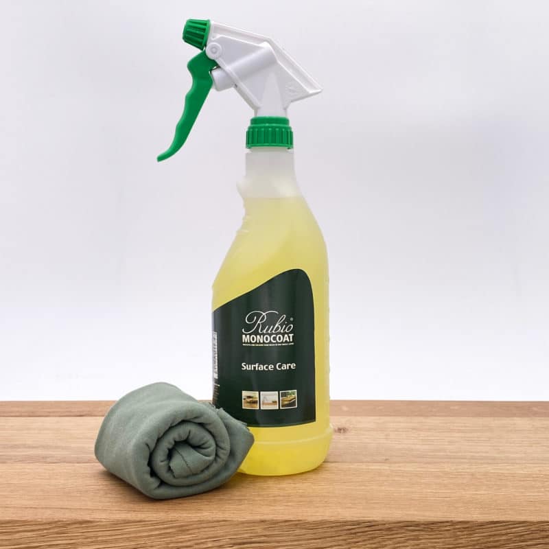 Reinigungsflasche und Tuch zur Holzpflege auf Holzoberfläche.