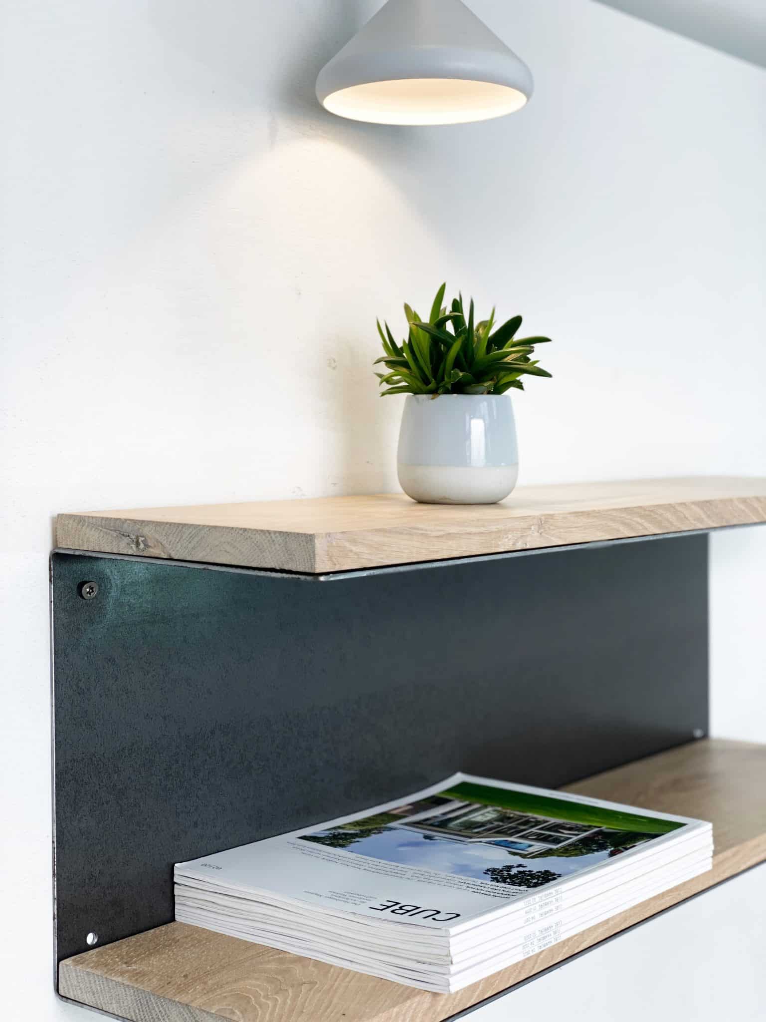 Eine schlichte Wandkonsole mit einer hellen Holzplatte trägt eine kleine Pflanze in einem weißen Topf und wirkt modern und reduziert.