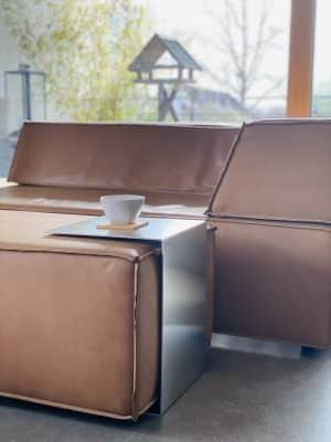 Ein braunes Ledersofa wird von einem modernen Metall-Beistelltisch mit einer Kaffeetasse ergänzt.