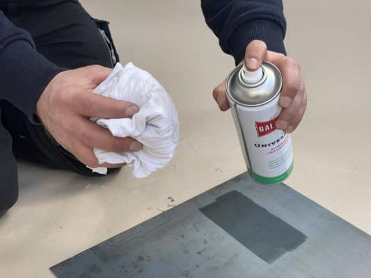 Eine Person reinigt eine Metallfläche mit einem Tuch und aufgesprühtem Reiniger.