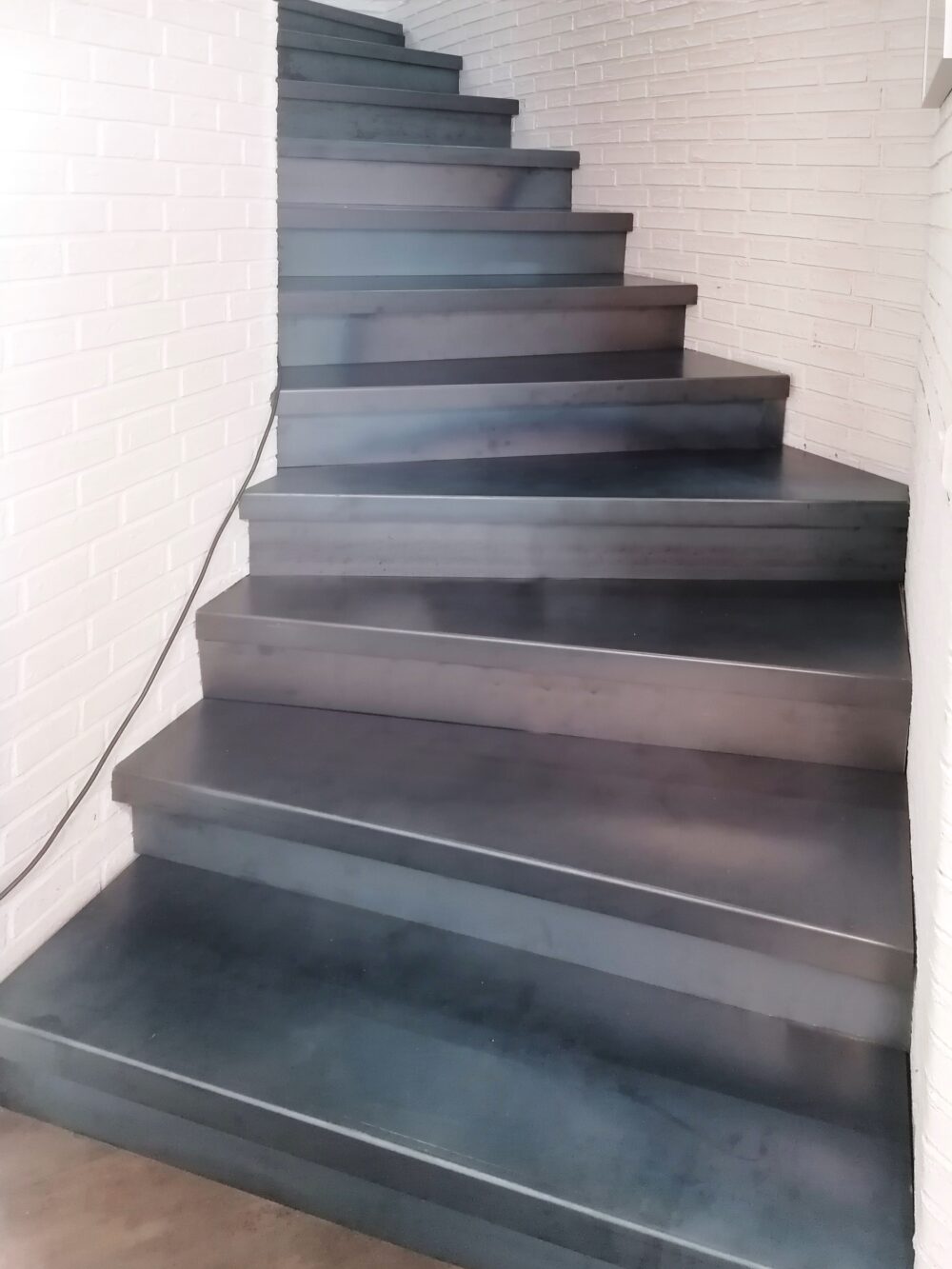 Schwarzstahl verkleidete Treppe mit weißen Backsteinwänden im Innenraum.