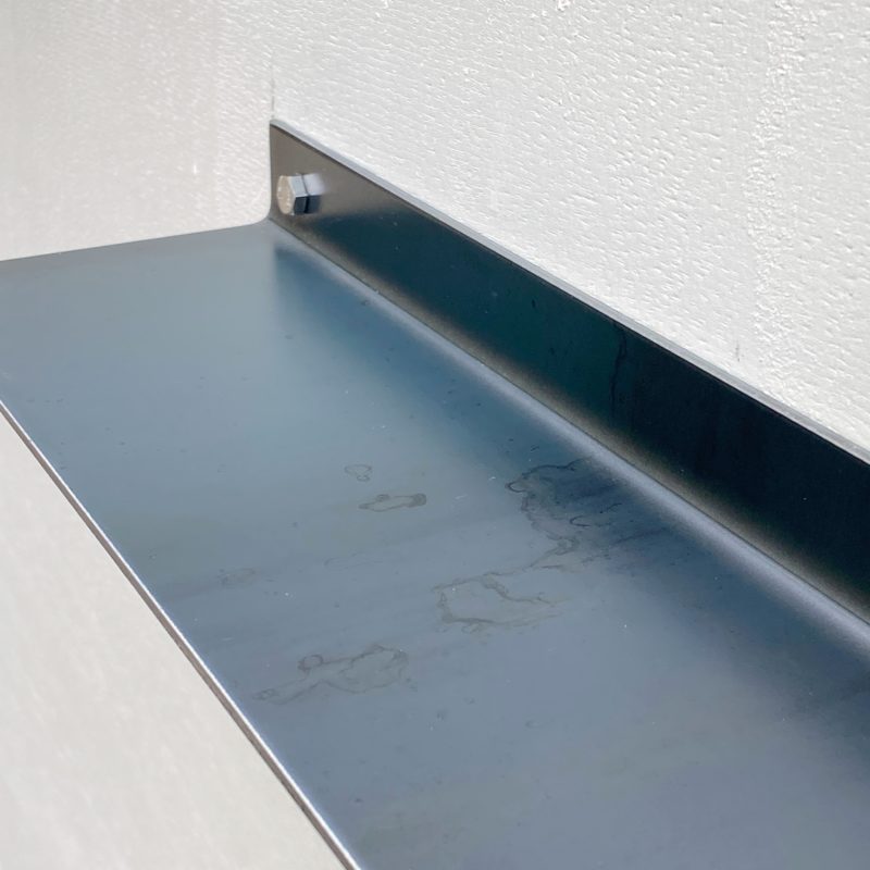 Nahaufnahme eines schlichten schwarzen Metallregals an weißer Wand.