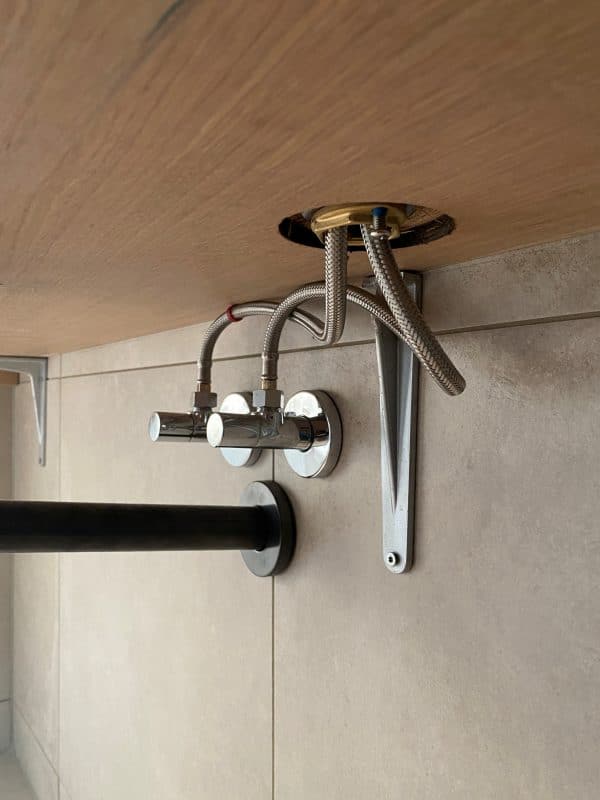 Mehrere Metallschellen und Leitungsanschlüsse sind unter einer Holzplatte montiert.