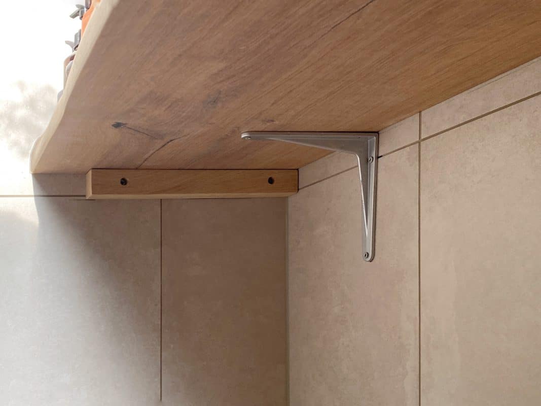 Eine Wandkonsole aus Metall trägt eine helle Holzplatte in einer minimalistischen Einrichtung.