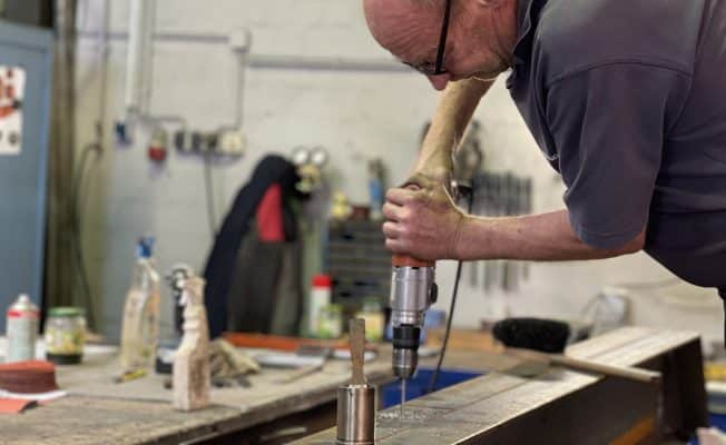 Ein Werkstatt-Mitarbeiter bohrt präzise ein Loch in einen Metallträger.