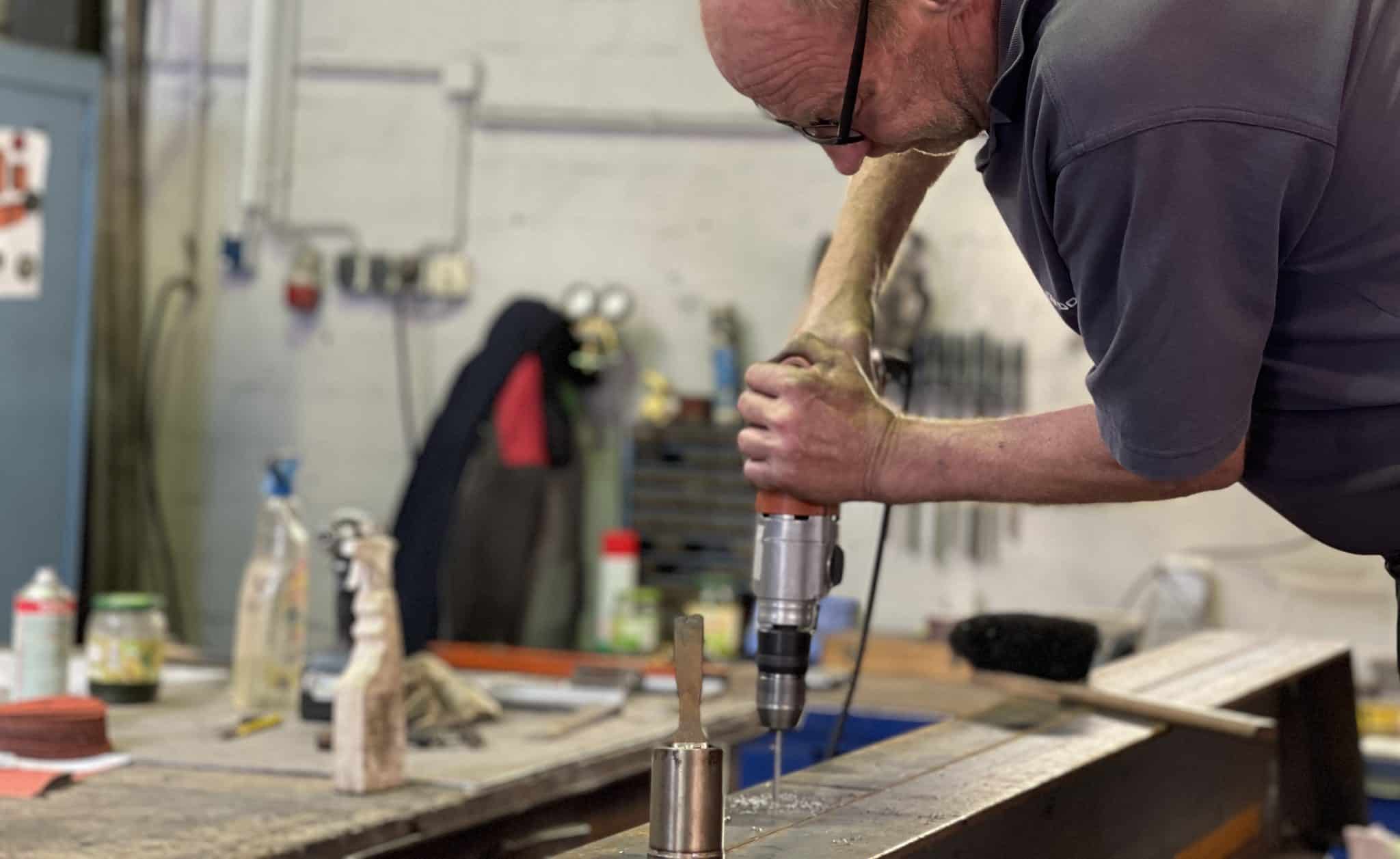 Ein Werkstatt-Mitarbeiter bohrt präzise ein Loch in einen Metallträger.